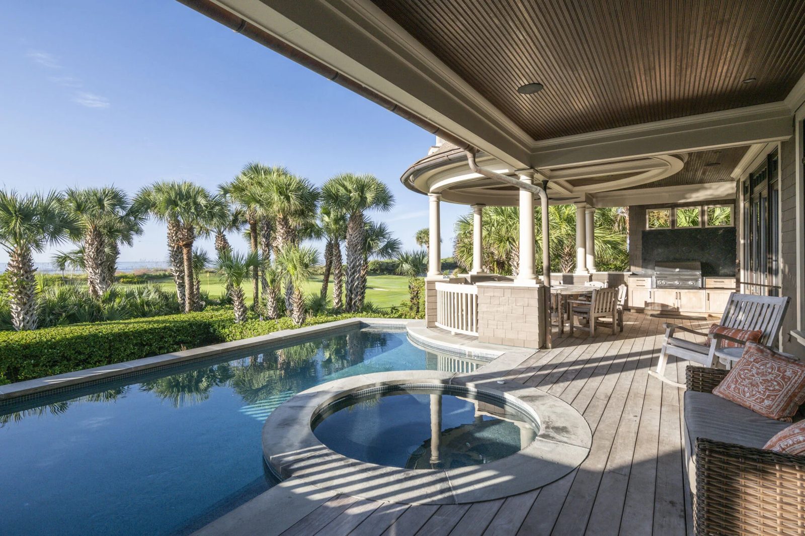 A covered porch beside a pool and spa, looking across palmettos to a golf green and the ocean