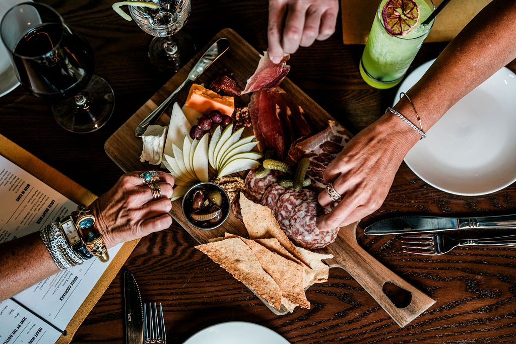 Hands reaching across a charcuterie board at Lou Lou's Tavern on the Tracks in Charleston