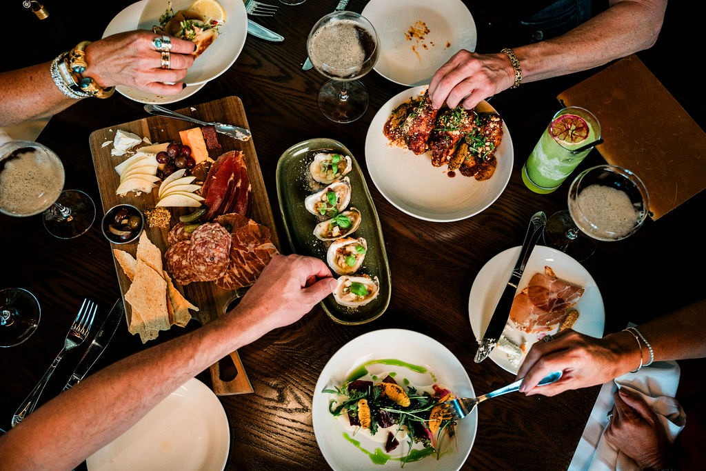 An overhead view of a shared table at Lou Lou's Tavern on the Tracks, hands reaching across boards and plates