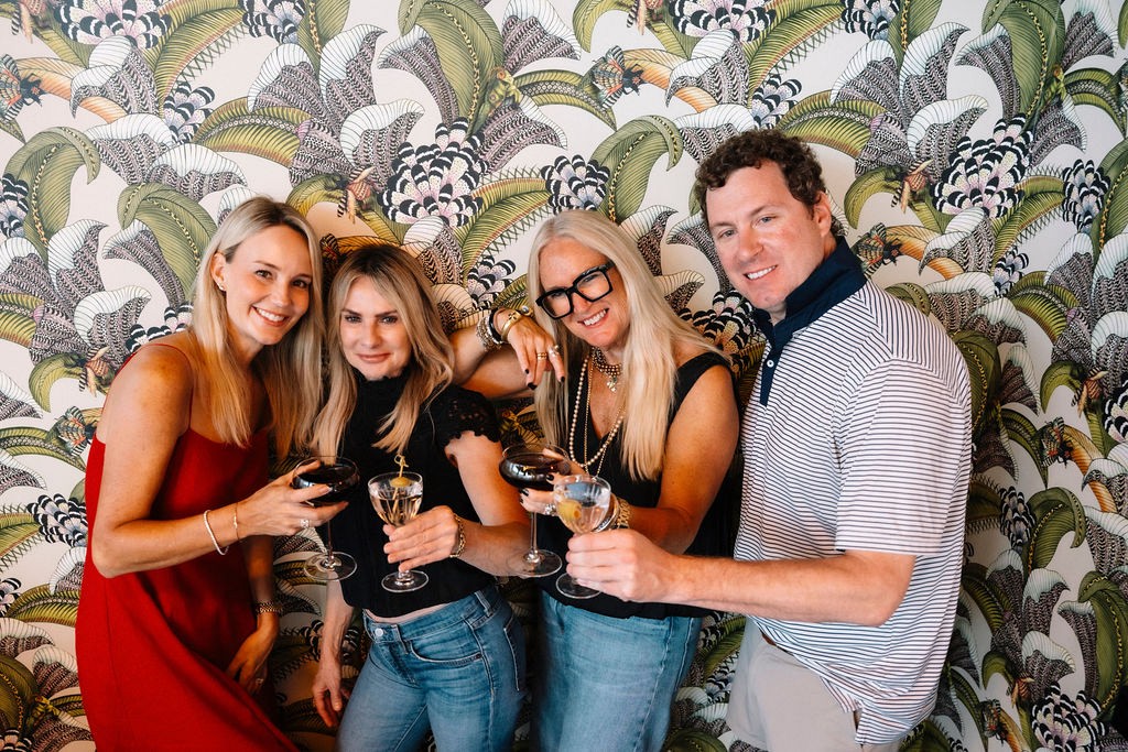 Four people raising glasses together against the palm print wallpaper at Lou Lou's Tavern on the Tracks in Charleston