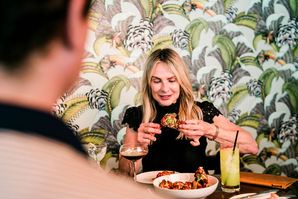 A guest eating at a booth against the palm print wallpaper at Lou Lou's Tavern on the Tracks