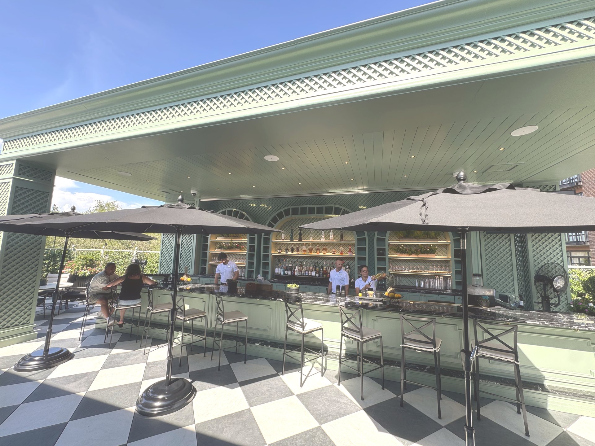 The Perch bar at The Charleston Place with sage green lattice, marble counter and bartenders working under canvas umbrellas