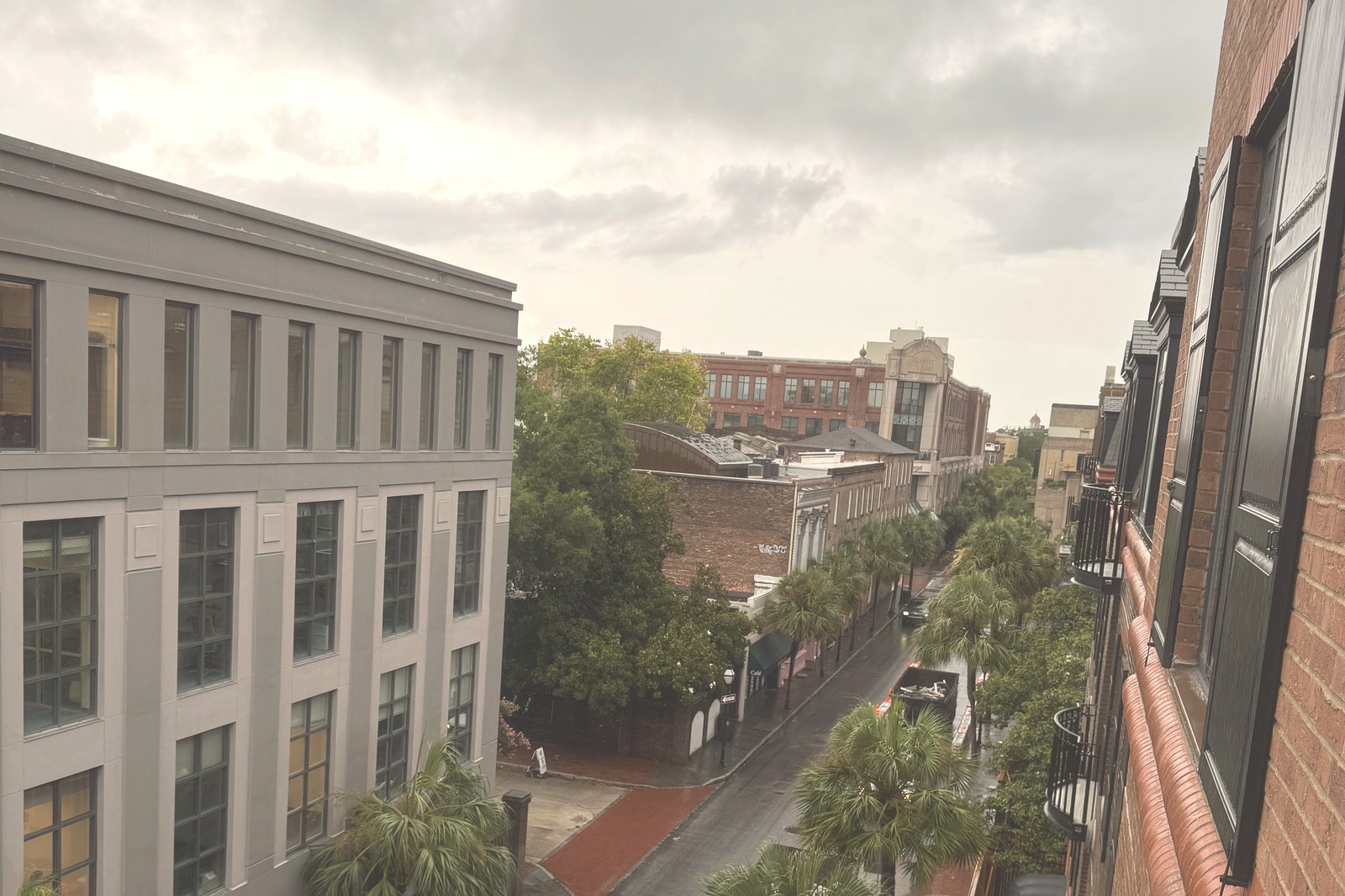 The view from the balcony of a Premier Balcony Room at The Charleston Place, looking down a wet Charleston street lined with palms