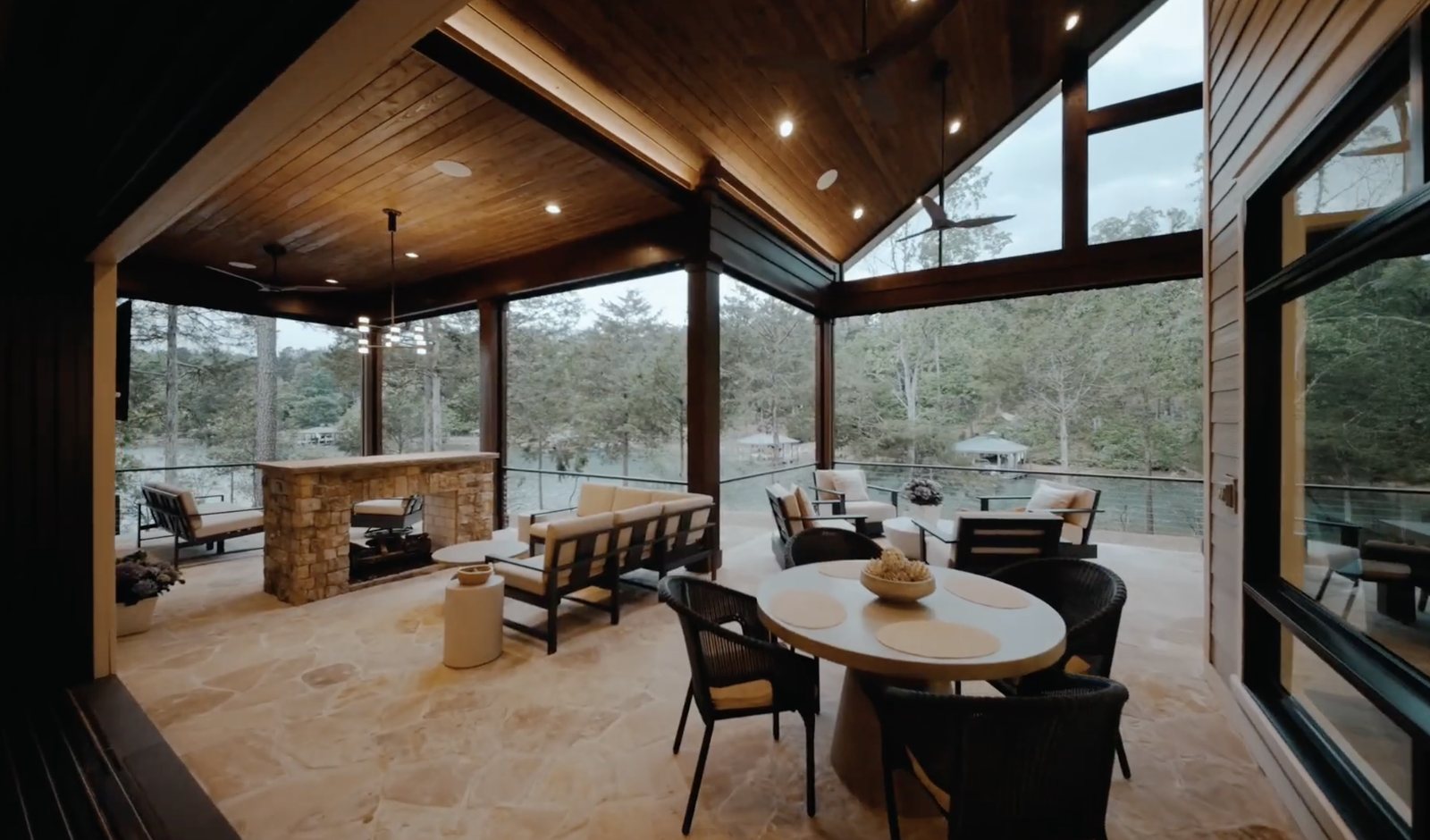 Covered lakeside living room with a stone fireplace, retractable screens and dining for a crowd, looking down the cove