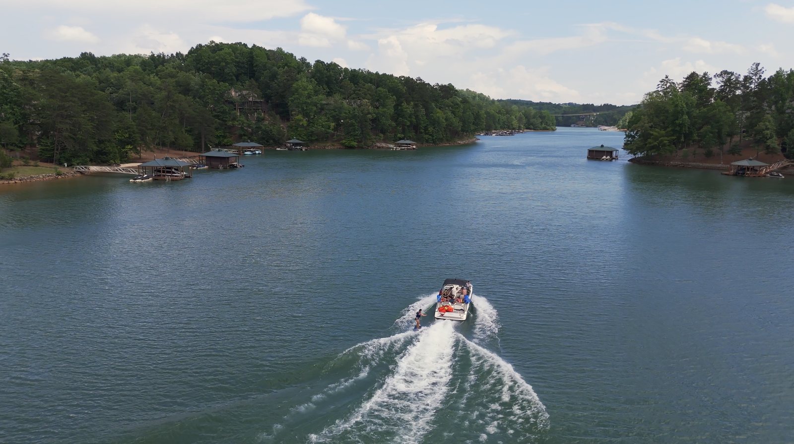 A wakeboarder behind a boat on open water on Lake Keowee, covered docks along both shores