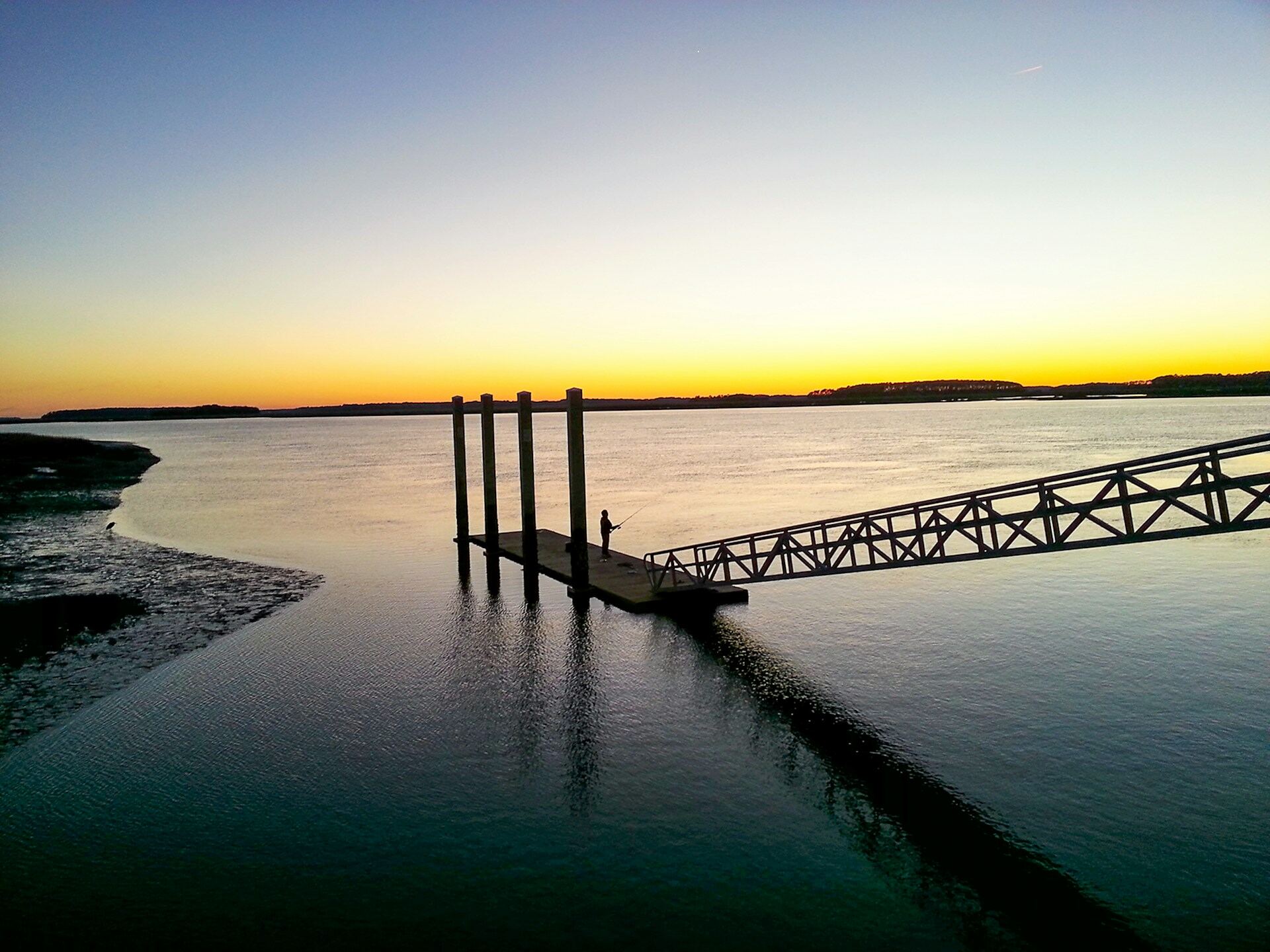 A dock running out into still water at sunset