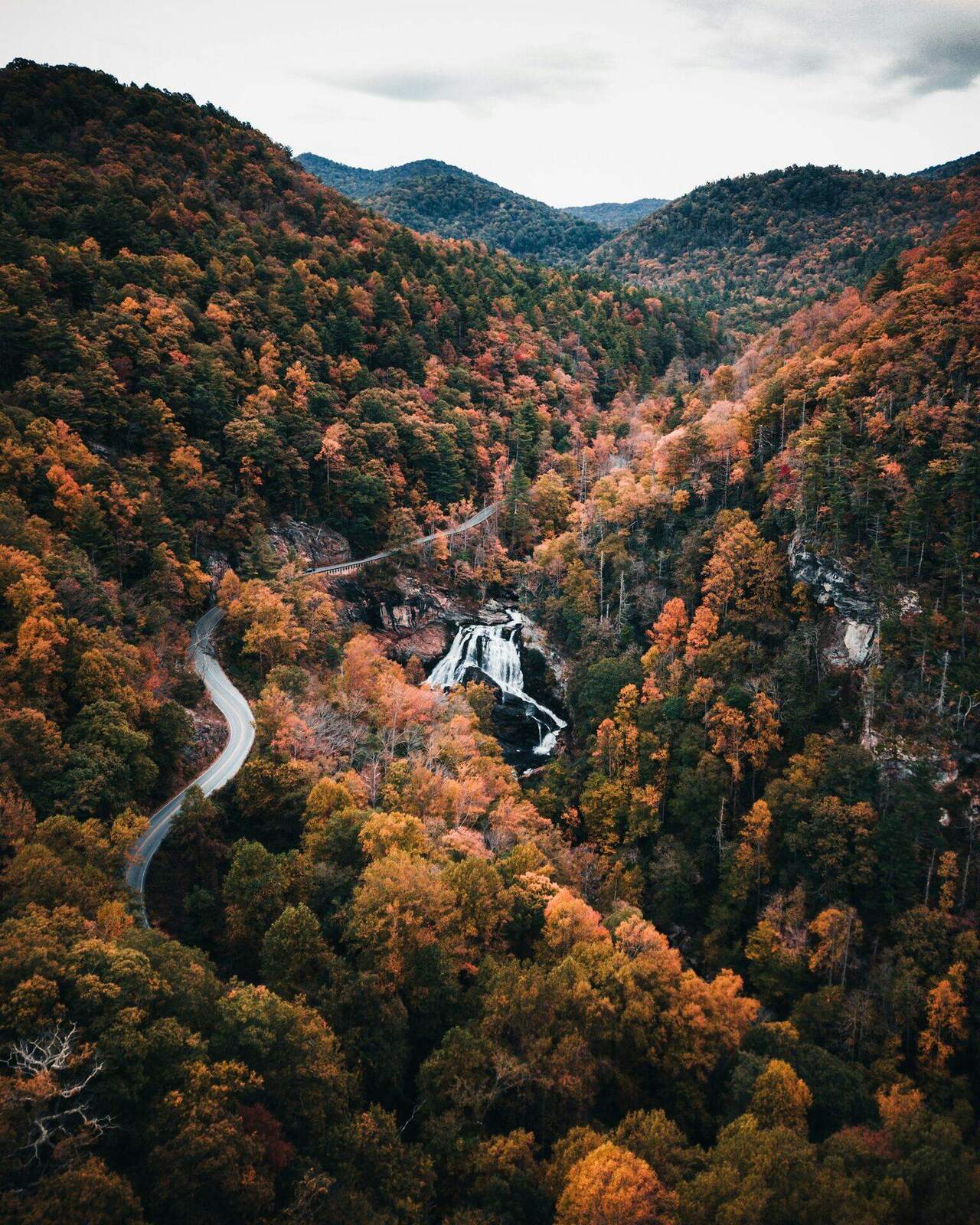 A waterfall and a winding mountain road seen from the air in autumn