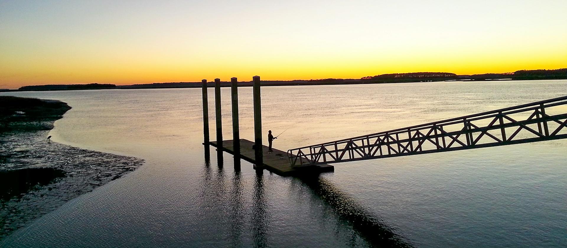 A dock reaching into still water at sunset on Hilton Head Island