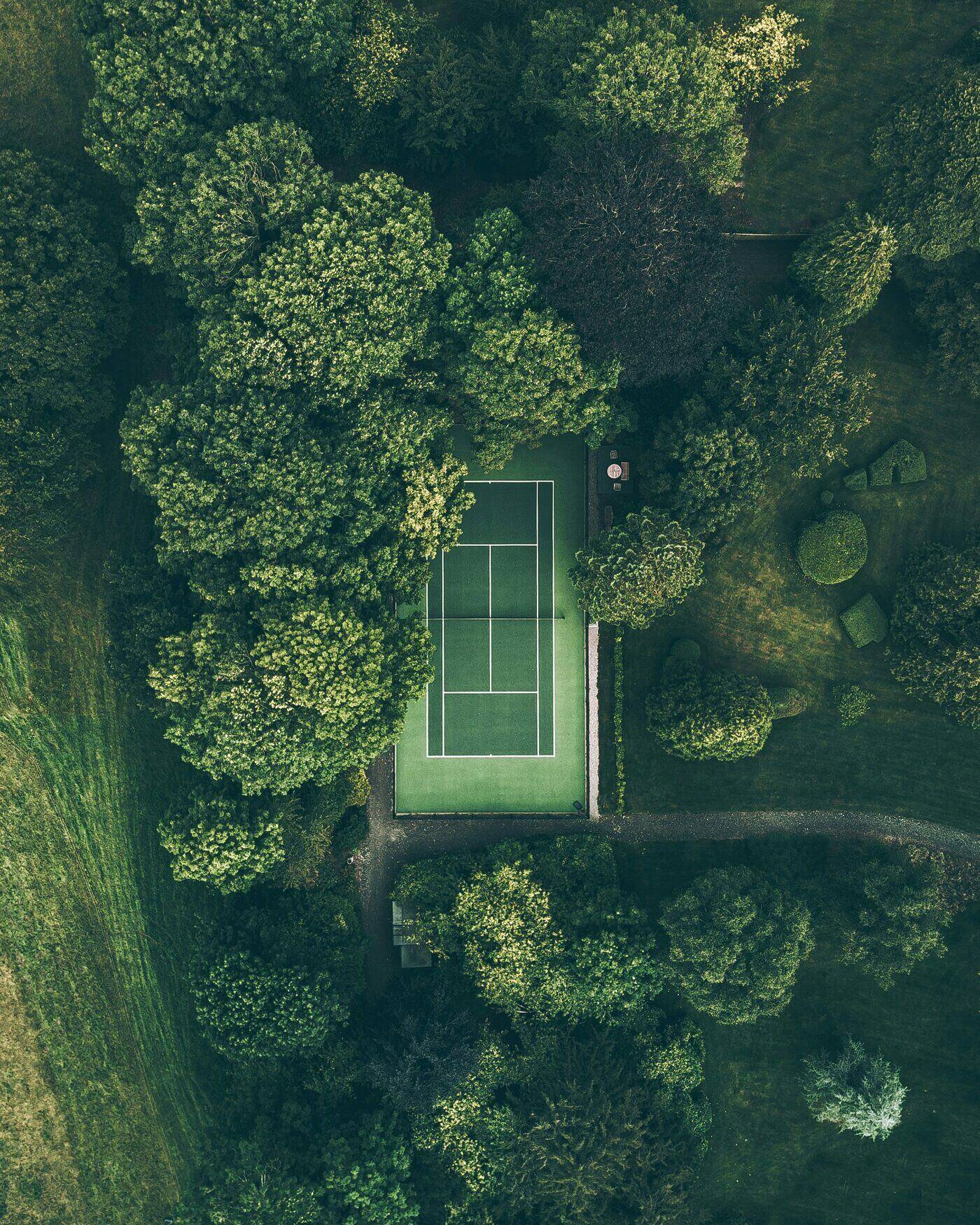 A private tennis court cut into dense forest, seen from above